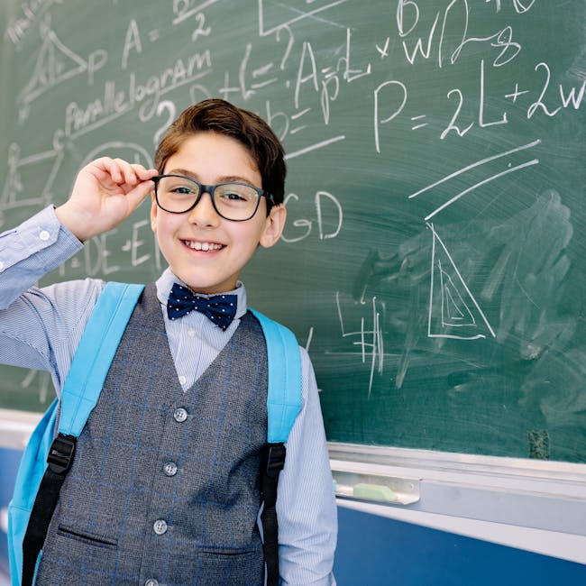 Smiling boy in a bowtie stands by a blackboard with math equations, wearing glasses and a backpack.